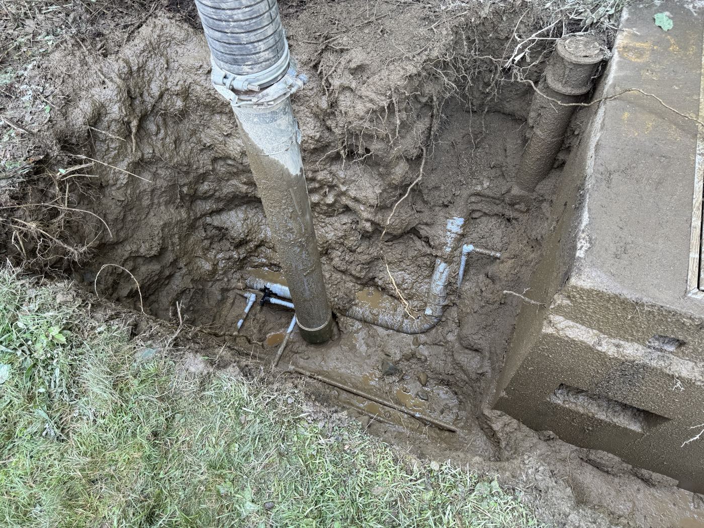 Vacuum-excavated pit exposing buried sense lines beside a regulator station vault